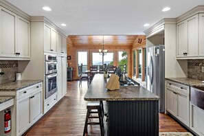 A kitchen with wooden cabinets, a central island, stainless steel appliances, and a fire extinguisher. - Blue Ridge Bliss | Mountain Home with Hot Tub & Stunning Views! (Weaverville)