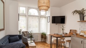 A modern living room with a sofa, a dining table, and a kitchen area with a bar stool.