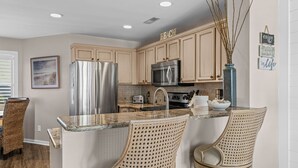 Una cocina con armarios color beige, electrodomésticos de acero inoxidable y una barra de desayuno con dos sillas de mimbre.