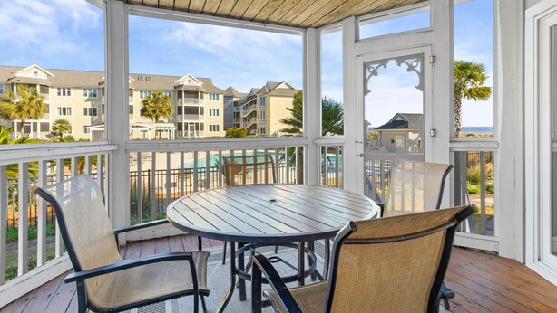 Un espacio al aire libre cubierto con una mesa redonda y sillas, con vistas a una zona residencial con varios edificios y al mar.