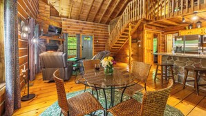 A wooden cabin interior with a dining area, kitchen, and a staircase leading to an upper level. - Rustic Cabin Getaway with Hot Tub, Trails & Fire Pit (Logan)