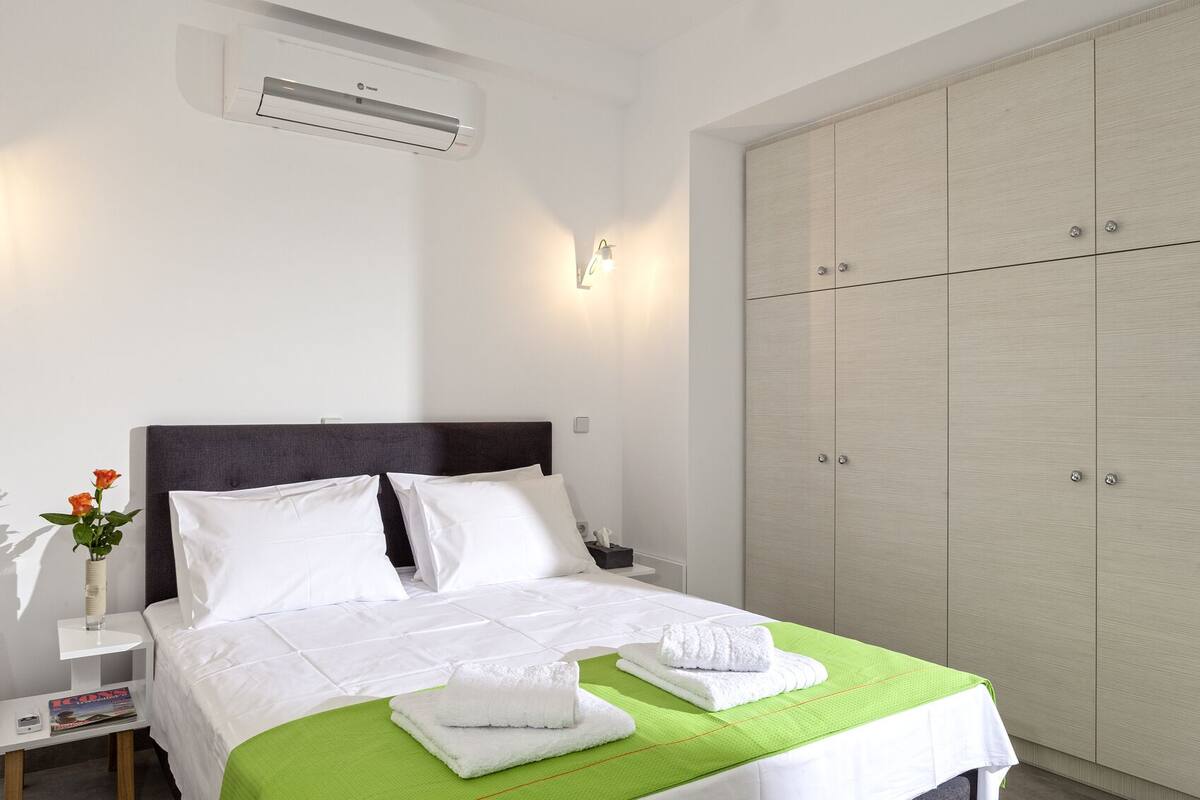 A hotel room with a bed, a nightstand, a green towel, a white vase with flowers, and a wardrobe.