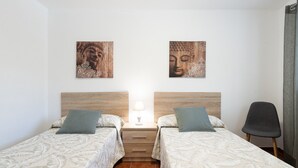Una habitación con dos camas, una mesita de noche con lámpara y dos obras de arte colgadas en la pared.