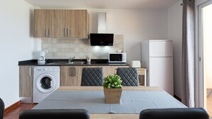 Una cocina moderna con armarios de madera, microondas integrado, lavadora y comedor con mesa y sillas.