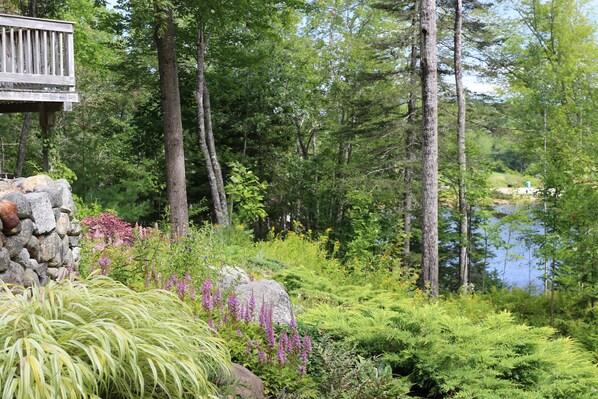 A wooden deck with a stone wall, surrounded by lush greenery and a lake.