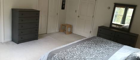 A bedroom with a bed, two dressers, a small stool, and a window with a view.
