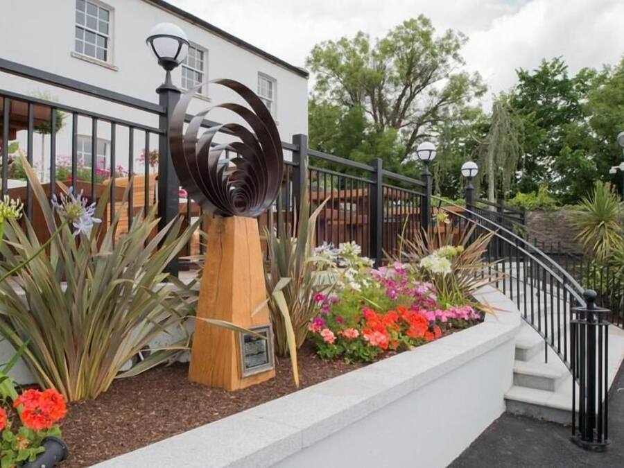 Ein Garten mit einer spiralförmigen Metallskulptur, einer hölzernen Bank und einer Vielfalt bunter Blumen.