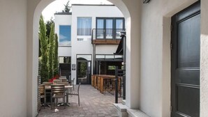 Un bâtiment moderne doté d’une cour intérieure, comprenant un banc et des chaises en bois, une petite table et une porte donnant sur un balcon.