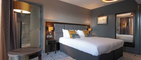 A hotel room with a large bed, bedside tables, a chair, a desk, and a mirror.