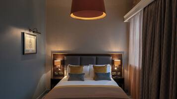 A modern hotel room with a large bed, a headboard with integrated lighting, a hanging pendant light, and a framed picture on the wall.