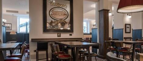 Un restaurante con varias mesas y sillas, un cuadro en la pared y una alfombra estampada.
