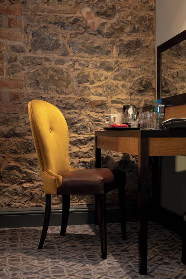 Un comedor con pared de piedra, una mesa de madera, una silla tapizada en amarillo y un suelo estampado.