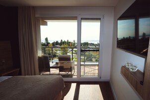 Quarto de hotel com cama, varanda com mesa e cadeiras e uma TV fixada na parede.