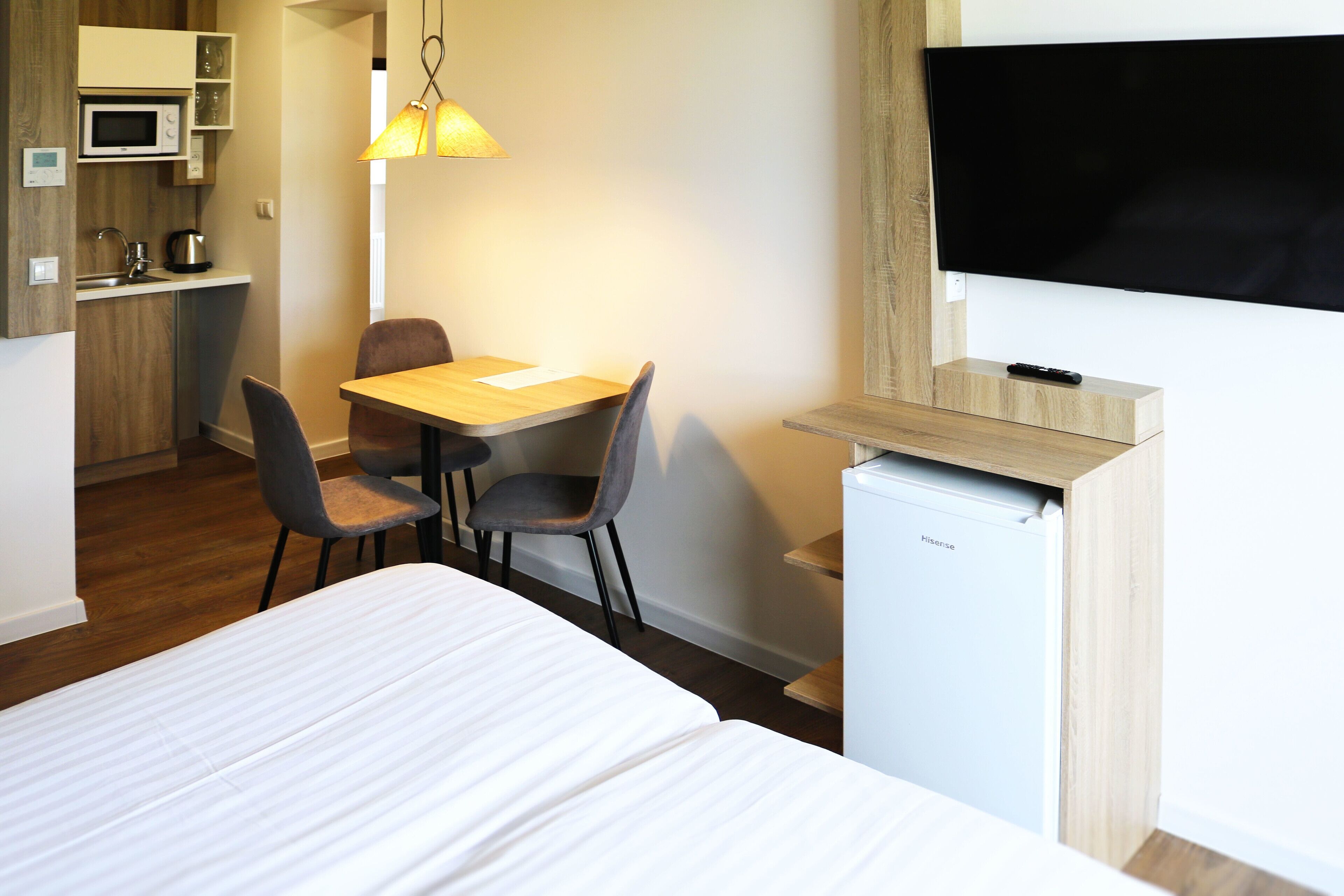 Ett hotellrum med en säng, ett skrivbord med två stolar, ett litet pentry, en tv och ett kylskåp.