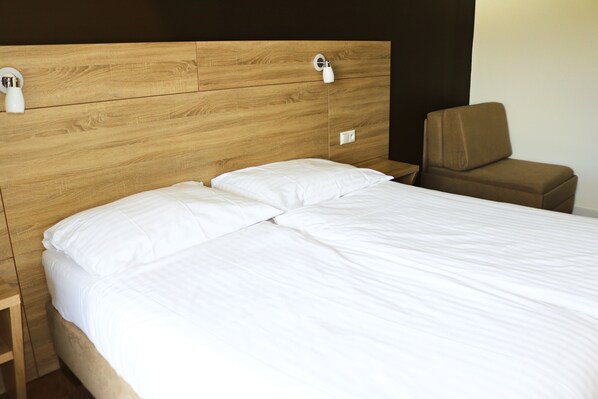 Una cama bien hecha con sábanas blancas, un cabecero de madera y un sillón marrón.
