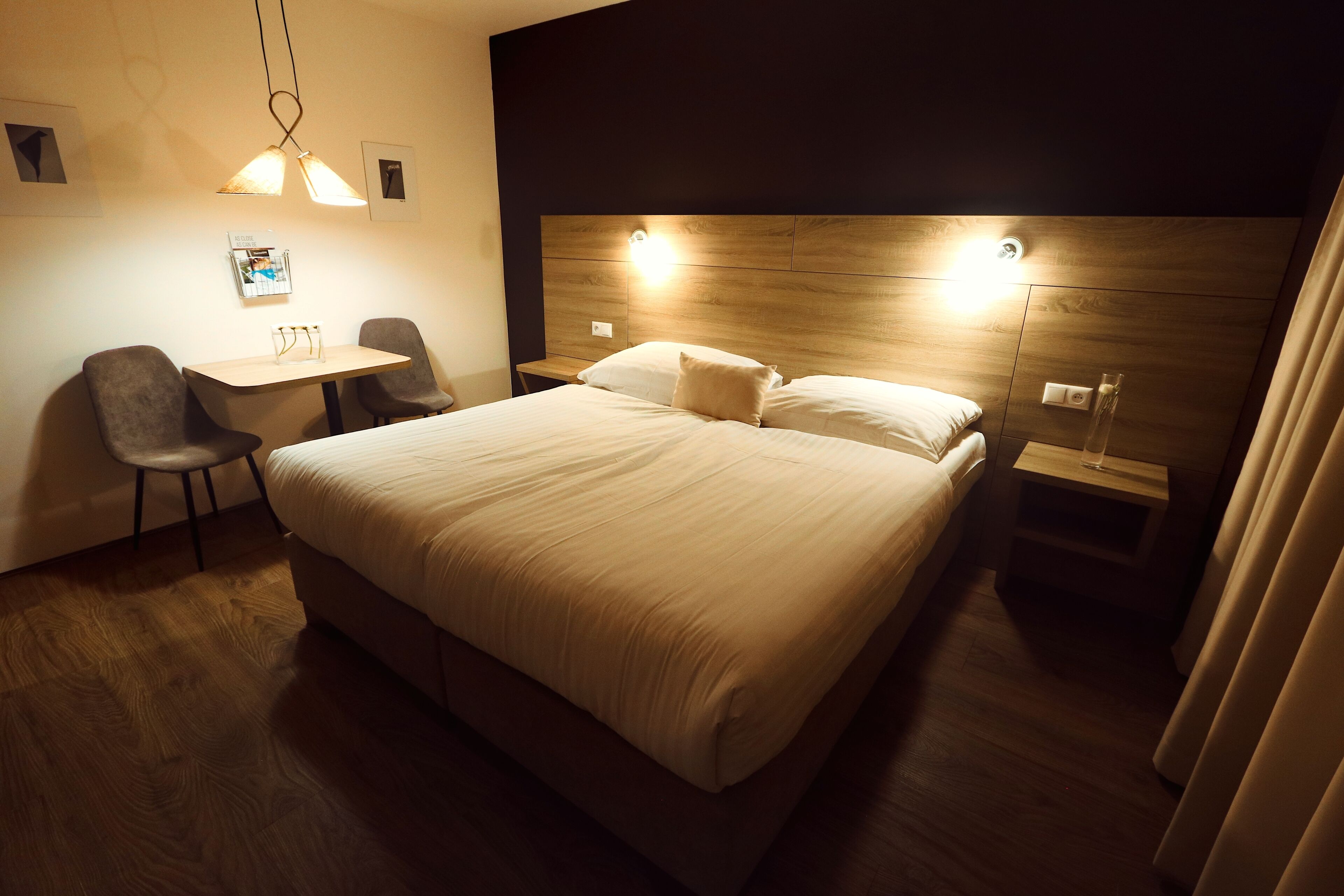 A hotel room with a large bed, a desk with two chairs, and a wooden headboard with integrated lighting.