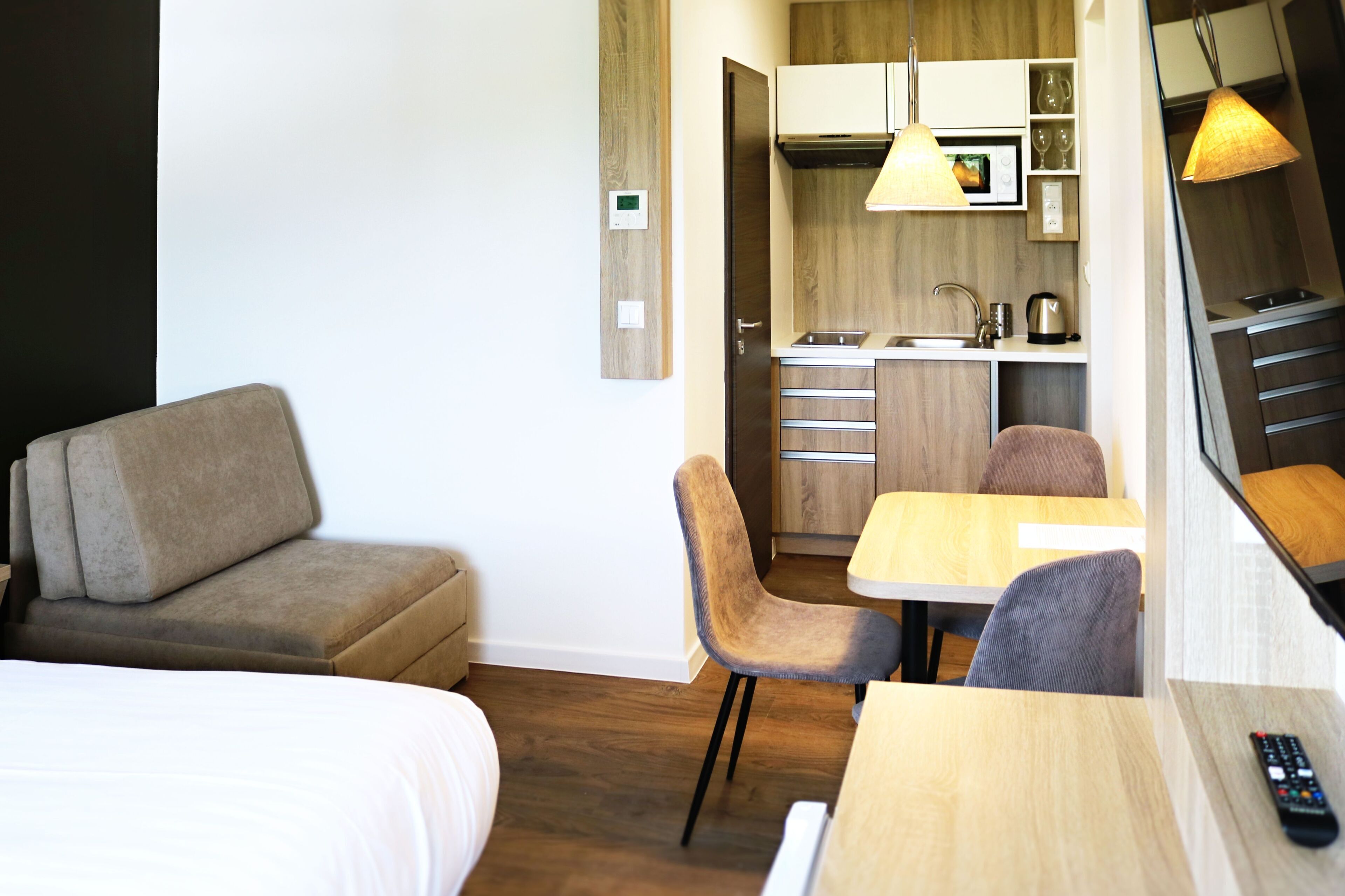 Habitación de hotel con cama, sofá, mesa de comedor con sillas, zona de cocina con microondas y lámpara colgante.