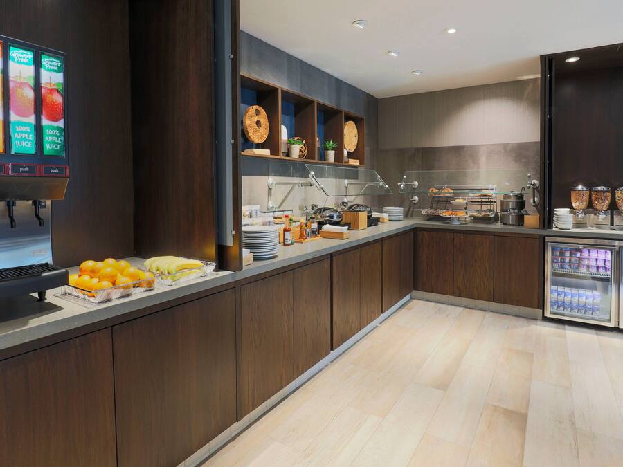 A modern breakfast bar with a juice dispenser, a variety of fruits, and a refrigerated display.