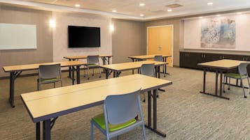 A conference room with multiple tables and chairs, a whiteboard, a flat-screen TV, and a large map on the wall.