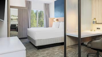 Habitación de hotel con cama, escritorio, silla y un amplio ventanal con vistas a árboles.