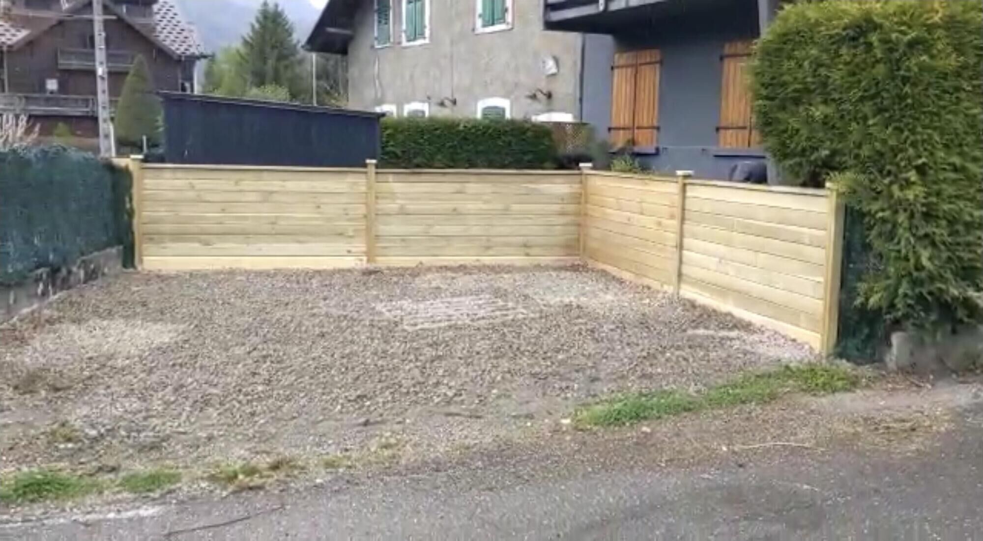 Spazio esterno recintato con fondo in ghiaia, circondato da edifici residenziali.