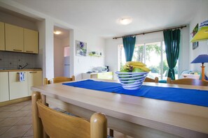 A dining area with a wooden table, chairs, and a blue placemat. There is a bowl of fruit on the table. - 4-room apartment 100 meters from the sandy beach. Air conditioning (Ghisonaccia)