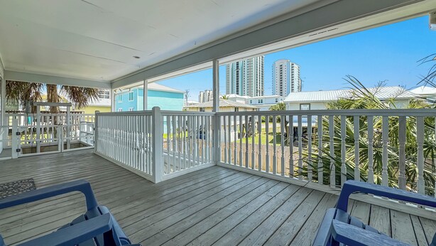 A covered outdoor area with wooden flooring, white railings, and blue chairs. - PRIVATE HOME, CLOSE TO THE BEACH, GREAT FOR FAMILIES, CONVENIENT TO EVERYTHING (Gulf Shores)