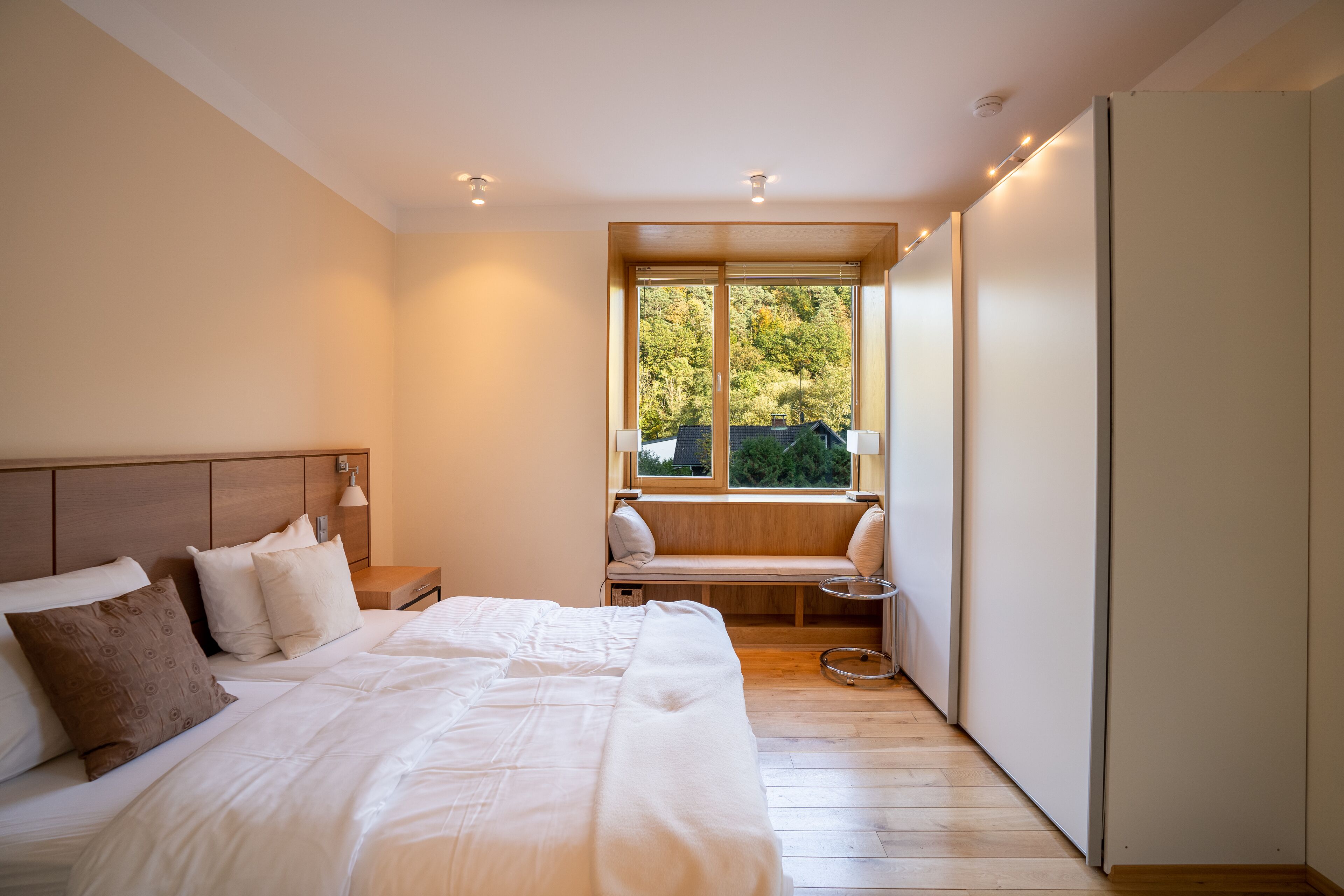 A bedroom with a large bed, a window seat, and a view of trees.
