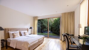 Un dormitorio con cama, escritorio y silla. Hay una ventana con cortinas y vistas a zonas verdes.