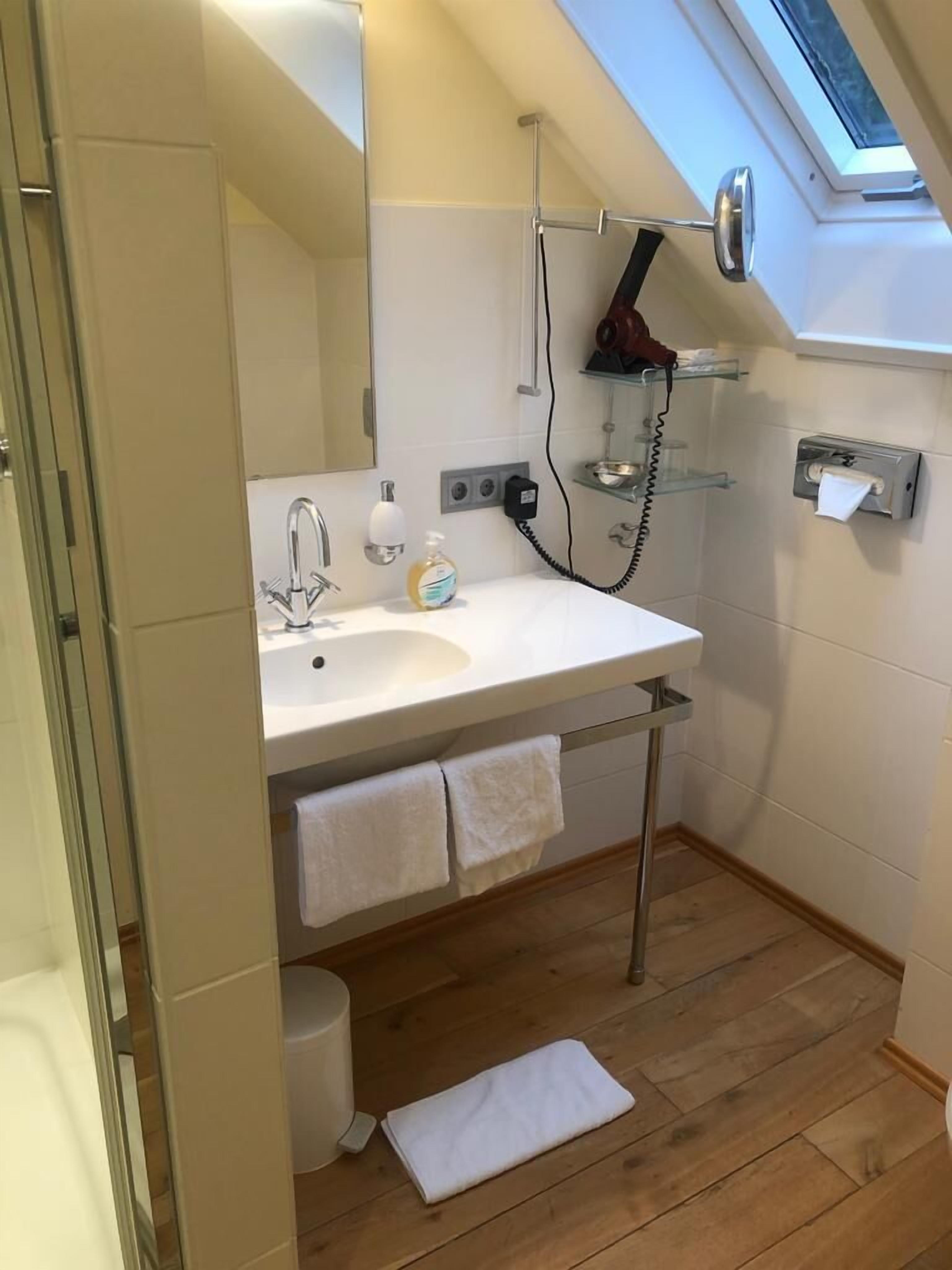 Un baño moderno con tragaluz, un lavabo con espejo, un secador de pelo y un perchero para toallas.