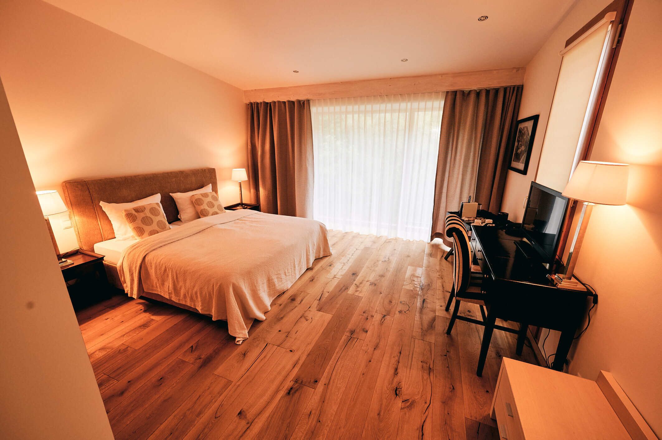 Una habitación de hotel con una cama grande, un escritorio con una silla, un televisor y una ventana con cortinas.