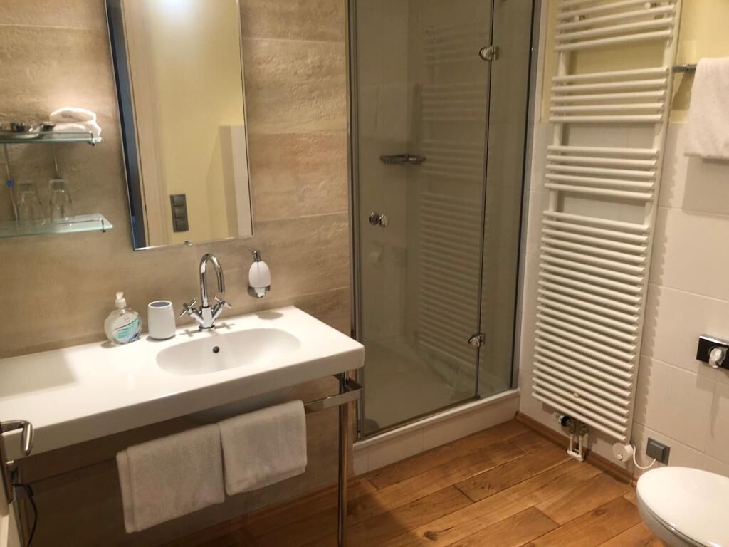 Un baño con cabina de ducha de vidrio, un lavabo blanco con espejo y un perchero para toallas.