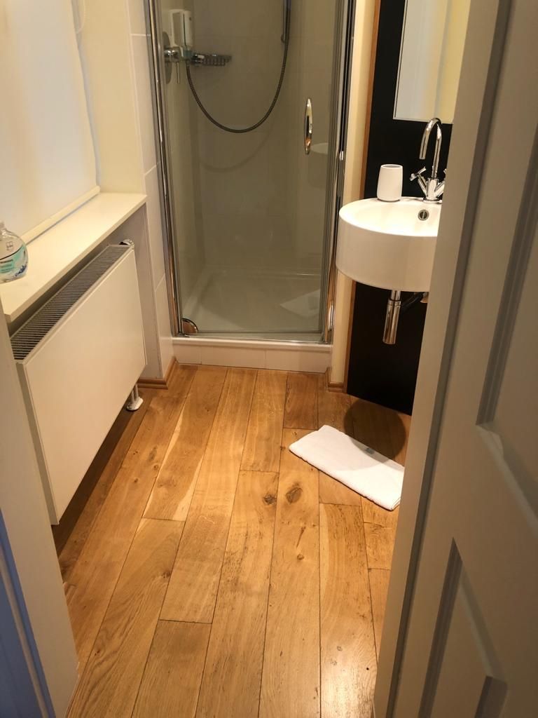 Une salle de bain avec une douche à parois de verre, un lavabo blanc et un plancher en bois.