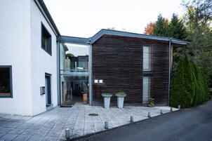 Um edifício moderno com entrada de vidro, fachada de madeira e duas plantas em vasos na calçada.