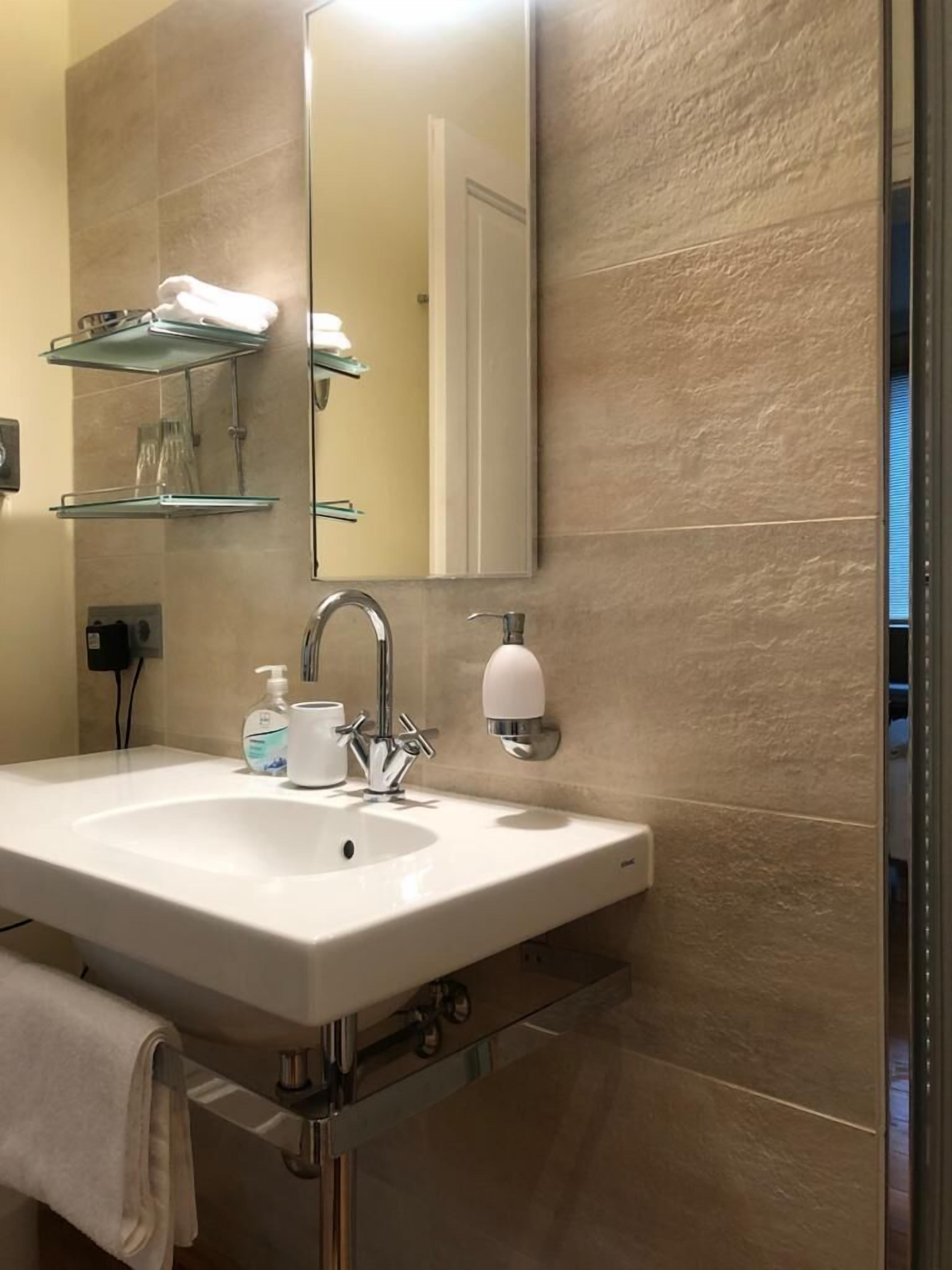 A bathroom with a white sink, a mirror, and a glass shelf above it.