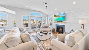 A spacious living room with a fireplace, comfortable seating, large windows, and a scenic view. - NEW LUXURY HOME, 2 houses from BEACH,5 Bedroom,Sleeps 12,Heated POOL, Game Room (Long Beach Township)
