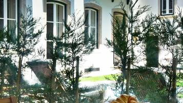 A breakfast table with a variety of food items and drinks, set against a backdrop of a building with a balcony and trees.