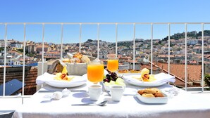 A breakfast table with plates of food, cups, and a glass of orange juice, overlooking a cityscape. - Casa Balthazar (Lisbon)