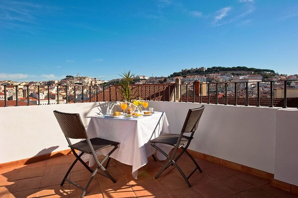 A terrace with a table set for two, overlooking a cityscape with buildings and a hill in the distance. - Casa Balthazar (Lisbon)