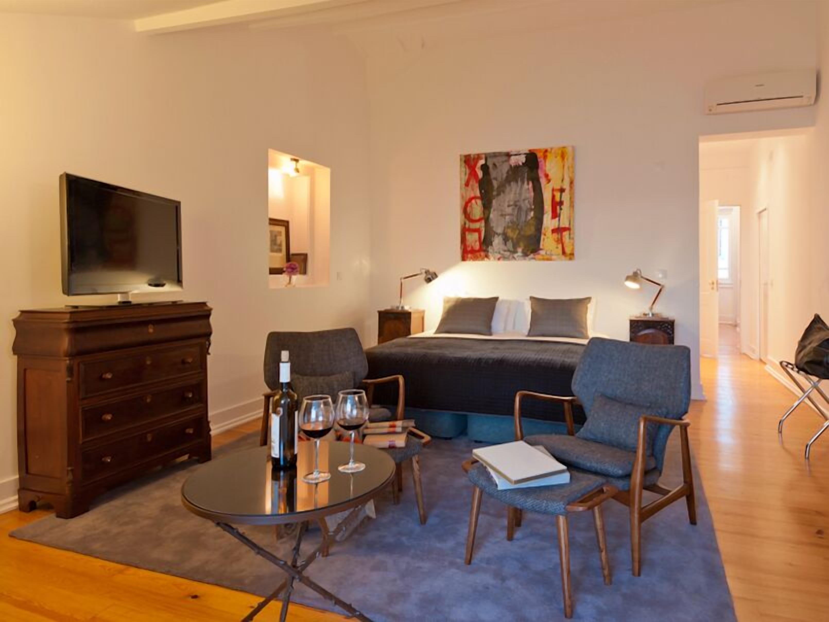 A modern bedroom with a bed, bedside tables, a TV, a coffee table, and seating area.