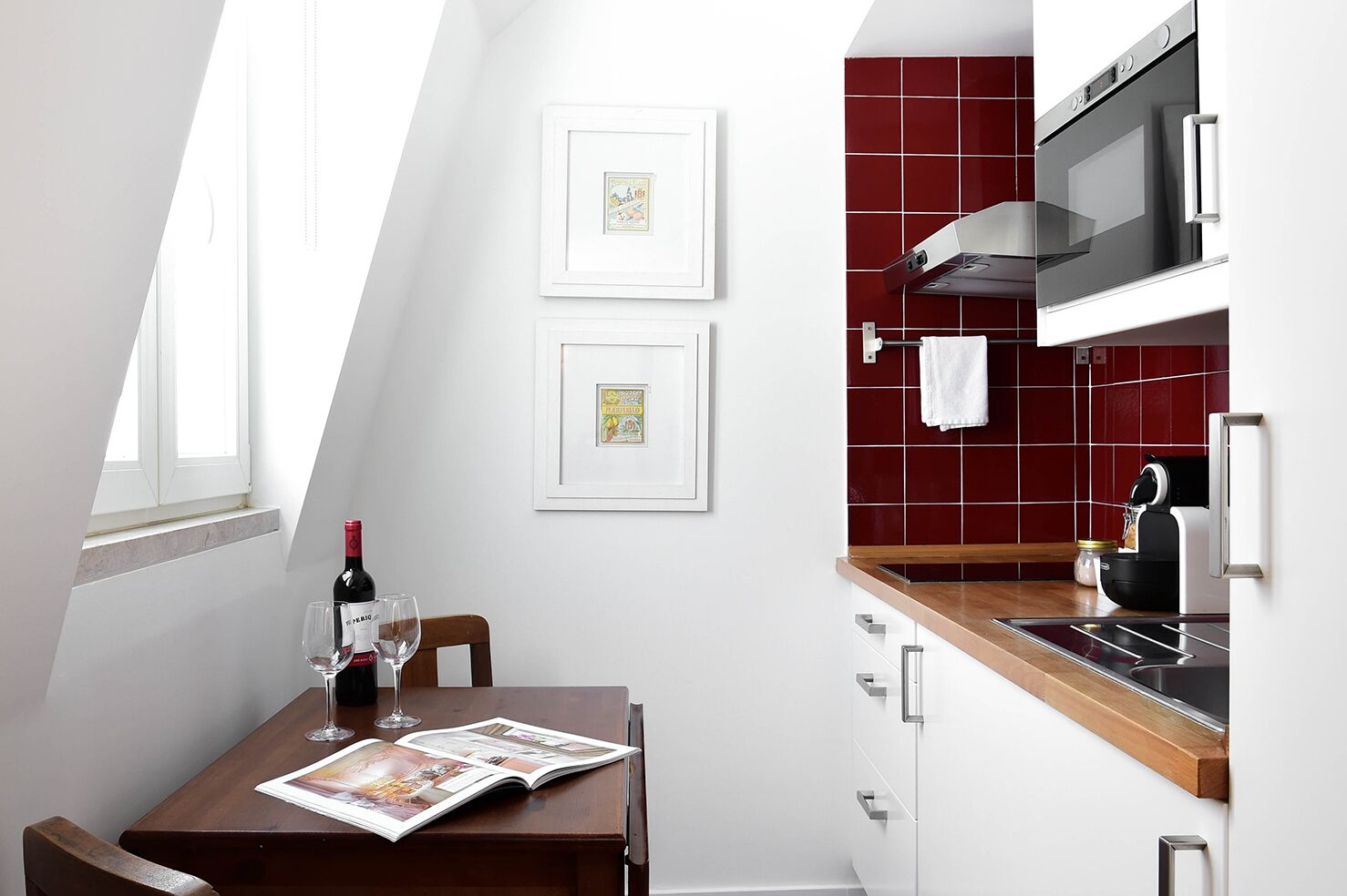 Eine moderne Küche mit roter Fliesenspiegel, Edelstahlgeräten und einer Essecke mit Tisch für zwei Personen.