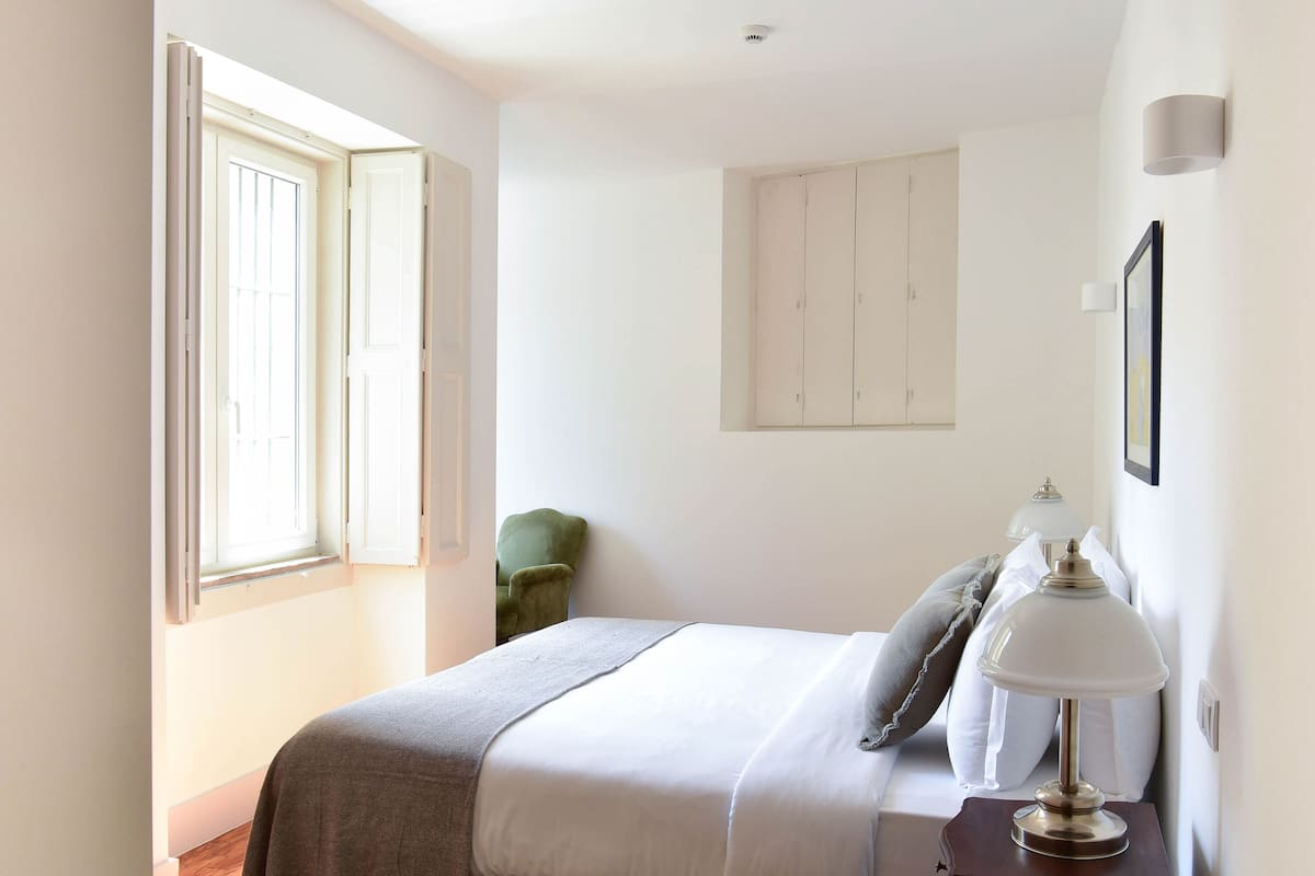 Un dormitorio con una cama, una mesita de noche con lámpara, una silla verde y un armario.