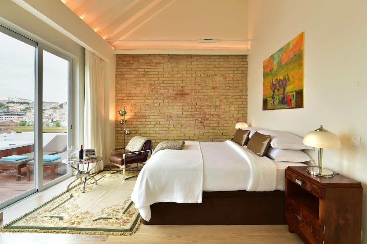 Habitación de hotel con una cama grande, un escritorio con silla, vista a través de un ventanal y una pared de ladrillo.