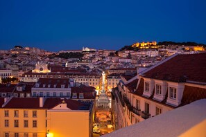 A cityscape at dusk with historic buildings, a prominent church, and a hilltop castle. - Casa Balthazar (Lisbon)