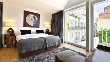 A modern hotel room with a large bed, two bedside tables with lamps, a view of the city through a large window, and a painting on the wall.