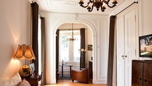A well-lit room with a chandelier, a television, a sofa, and a dining area with a table and chairs. - Casa Balthazar (Lisbon)