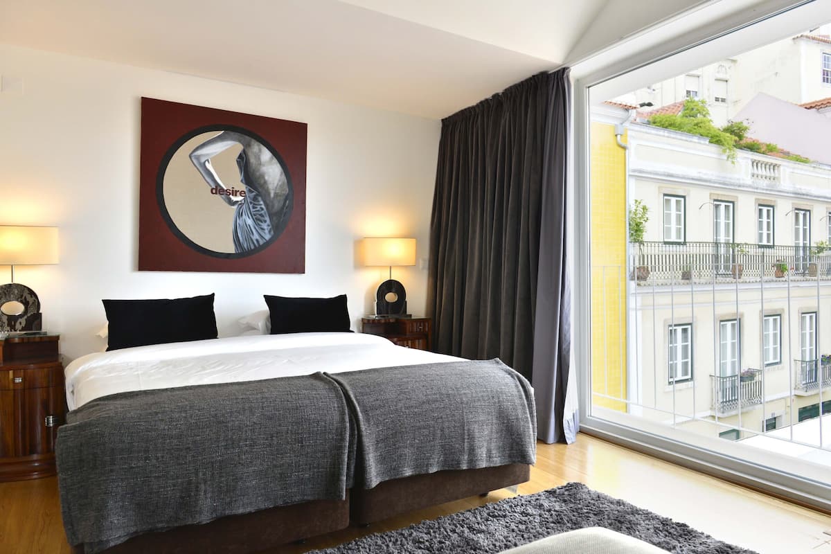 Habitación de hotel moderna con una cama grande, vistas a la ciudad y una obra de arte enmarcada en la pared.