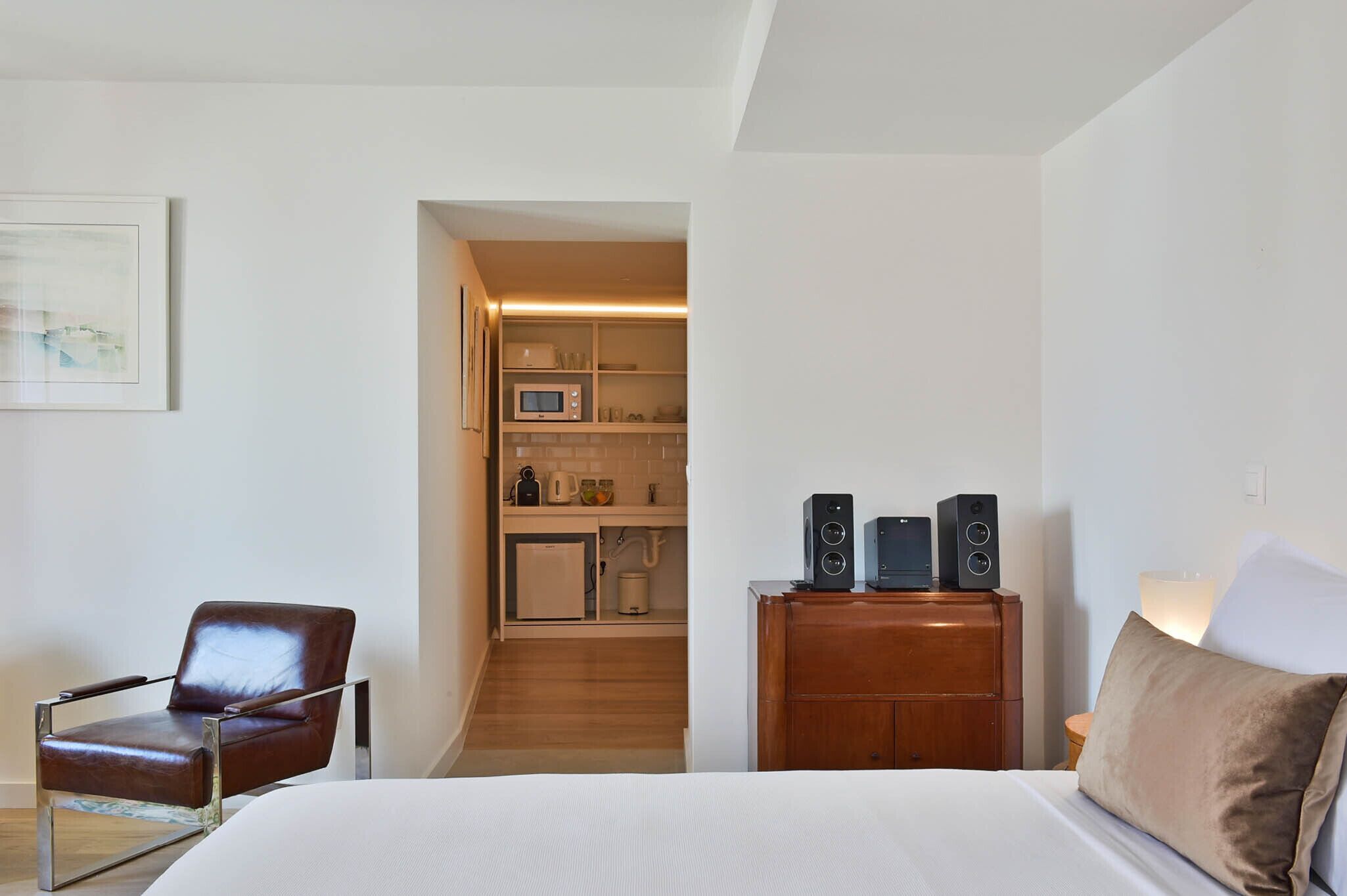 Een hotelkamer met een bed, een stoel, een houten dressoir en een kitchenette op de achtergrond.