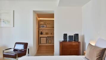Een hotelkamer met een bed, een stoel, een houten dressoir en een kitchenette op de achtergrond.