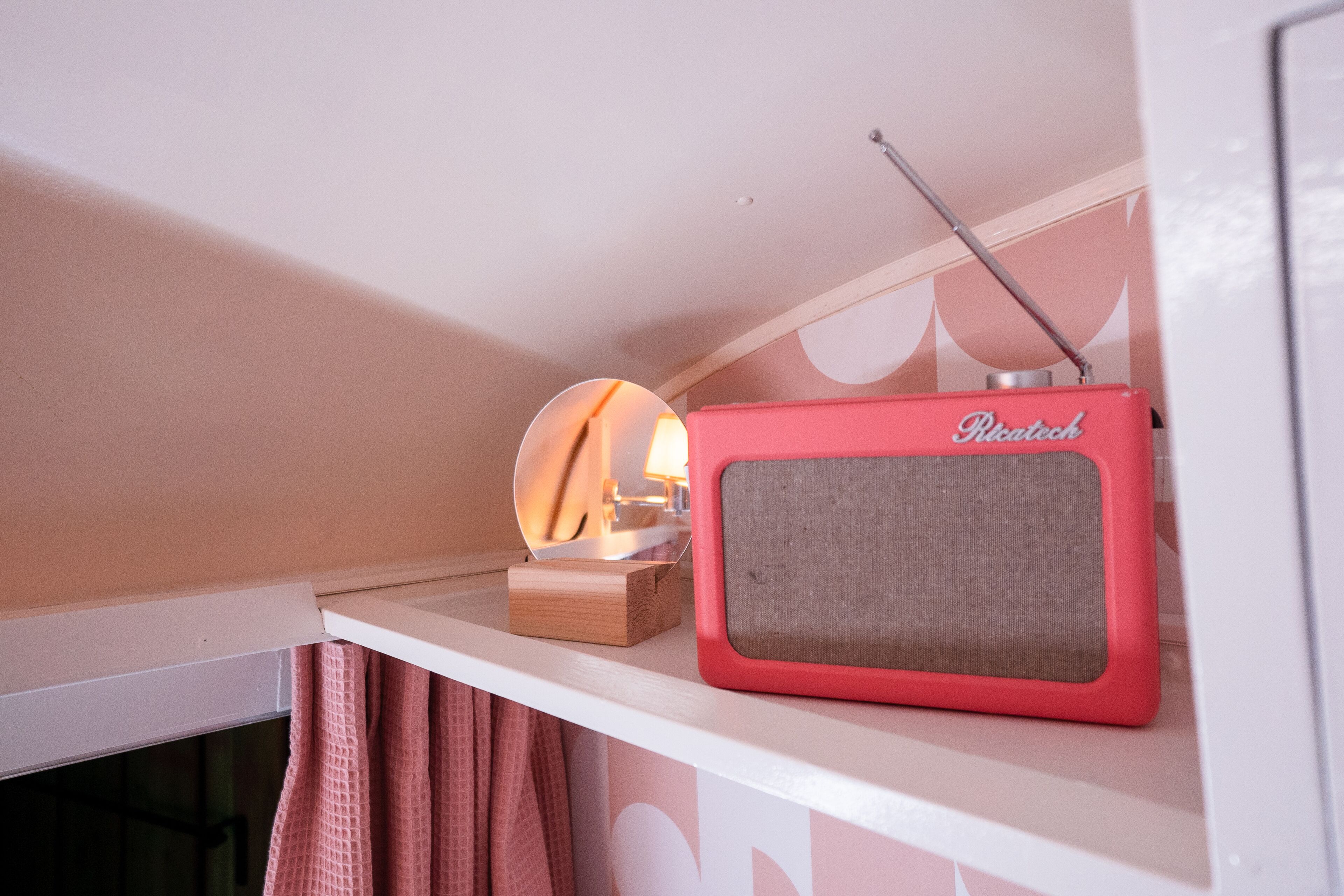 Une radio rose posée sur une étagère, à côté d’une boîte en bois et d’un miroir.